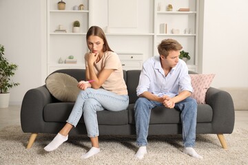 Worried couple with pregnancy test on sofa at home