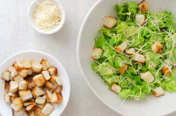 Traditional Caesar salad with croutons and parmesan cheese in a ceramic bowl on a gray table. Traditional American cuisine concept. Horizontal orientation. Selective focus. Top view.