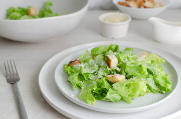 Traditional Caesar salad with croutons and parmesan cheese in a ceramic flat plate with ingredients on a gray table. Traditional American cuisine concept. Horizontal orientation. Selective focus.