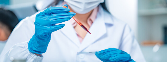 Female scientist in protective gear handling a blood sample in a laboratory, representing virus...