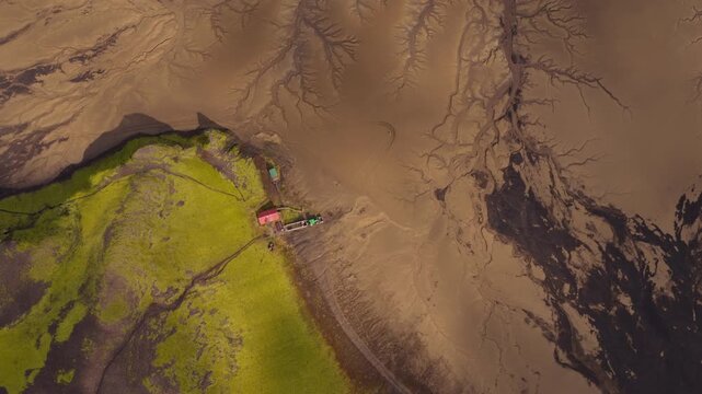 Aerial view of Iceland's brown terrain with intricate river channels and vibrant green vegetation, captured with gradual drone motion.