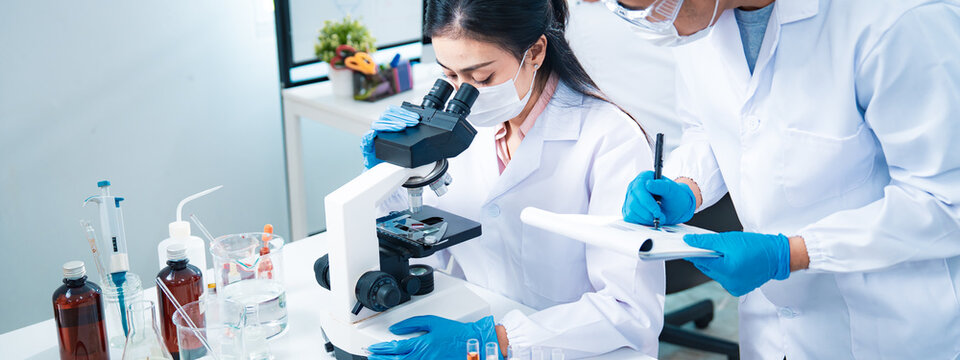 Team of scientists collaborating in a laboratory, with a female researcher using a microscope and a colleague recording notes, symbolizing teamwork, healthcare diagnostics, and innovation. - Powered by Adobe