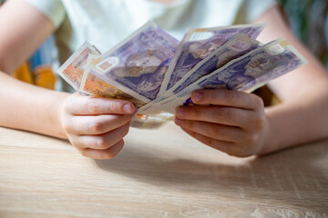 child 10 years old, primary school student presenting British GBP banknotes currency in hand,...