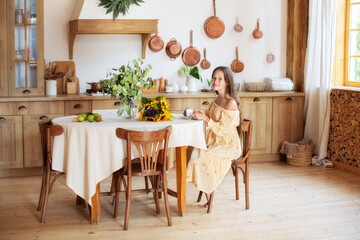 Portrait beautiful young girl in yellow dress sit on chair at table holding coffee cup and smiling at camera in cozy kitchen at home for relax, enjoy, peace or calm in morning.	
