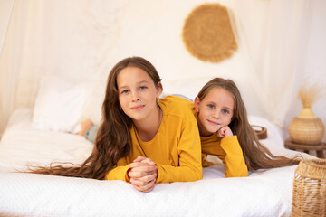 Happy family time concept. Sisters lie in bed at the morning and smiling in camera. Smiling teen girl with little sister siblings playing relaxing on the bed at home. Child friendship concept
