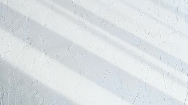 White plaster wall with rough texture and subtle shadows across the surface. The minimal background reflects modern design trends and is perfect for creative visual compositions.