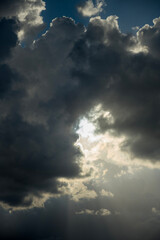 Obraz premium Dramatic sky with powerful sun rays breaking through dark storm clouds, creating an ethereal and atmospheric scene.