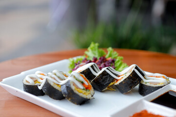 Close-Up of Fresh Japanese Maki Sushi Rolls on White Plate – Traditional Sushi with Vegetables and Sauce, Authentic Japanese Cuisine Served Outdoors © Bastera