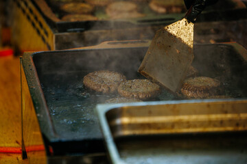 Juicy beef patties sizzling on grill under spatula at outdoor cookout