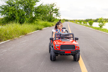 A cute little Asian girl is having fun riding her toy car on a rural paved road,A white baby...