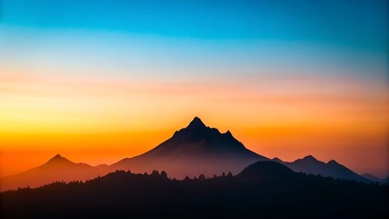 Silhouette of majestic mountain range against a gradient sunset sky with hues of orange, yellow, and blue