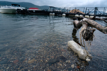 Plastic bottle pollution in lake water near dock, symbol of environmental problem and water...