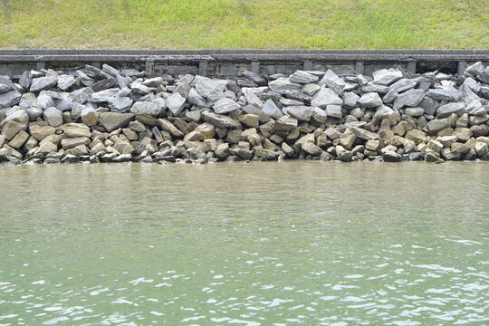 Riprap shoreline with stacked stones and calm green water along an embankment, erosion control structure forming rugged texture and pattern, natural waterfront background