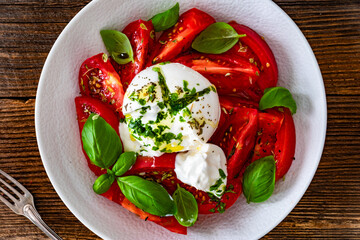 Caprese salad - tomatoes, fresh basil leaves and burrata cheese on wooden background	