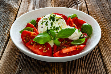 Caprese salad - tomatoes, fresh basil leaves and burrata cheese on wooden background	