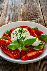 Caprese salad - tomatoes, fresh basil leaves and burrata cheese on wooden background	