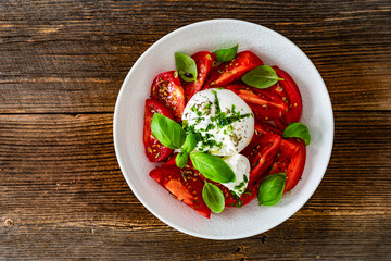 Caprese salad - tomatoes, fresh basil leaves and burrata cheese on wooden background	
