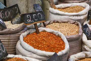 bags filled with different varieties of grains, with their respective prices on wooden boards, displayed in a traditional market