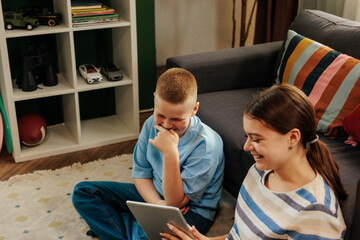 Generation Z siblings laughing while using tablet at home