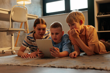 Gen z children watching tablet lying on floor at home