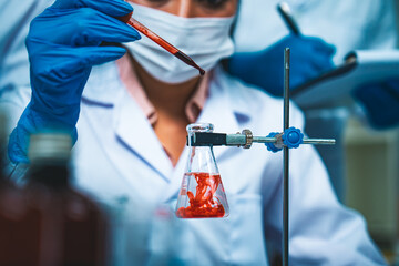 A scientist carefully drops a red solution into a flask, creating swirling patterns, symbolizing precision, innovation, and the critical role of laboratory research in advancing medical science.