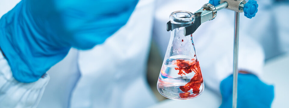 Close-up of a scientist dropping blood into a glass flask with precision, symbolizing research, biotechnology, and discovery in the pursuit of solutions for health, medicine, and science.