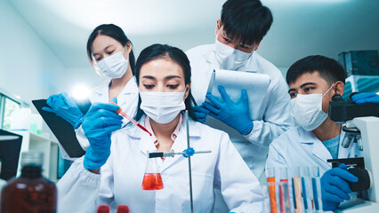 A group of scientists collaborate in a laboratory, with a female researcher dropping blood sample...