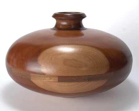 A lathe turned saucer vase.  The vase is narrow at the top and extends to an oval shape parallel to the horizon.  This is a piece of art.  The piece is centrally placed on white background.  - Powered by Adobe