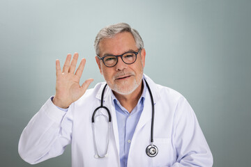 A healthcare professional waves during an online doctor consultation. He is wearing a white coat with a stethoscope around his neck, creating a welcoming atmosphere for patients.