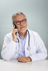 A healthcare professional is engaged in an online consultation, speaking on the phone while wearing a white coat. He looks attentive and approachable, providing medical advice remotely.