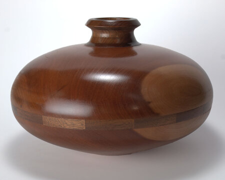 A lathe turned saucer vase. The vase is narrow at the top and extends to an oval shape parallel to the horizon. This is a piece of art. The piece is centrally placed on white background. - Powered by Adobe