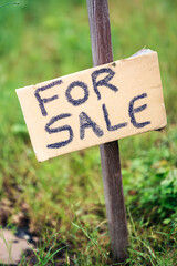 Rustic handwritten for sale sign in a green outdoor setting.