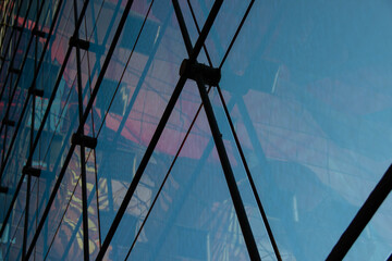 Abstract architectural detail showcasing glass reflections and structural elements, highlighting modern design with intersecting lines and vibrant colors in an urban environment