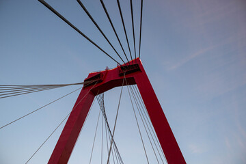 Fototapeta premium Red suspension bridge tower with cables extending towards the sky, showcasing modern engineering and architectural design against a serene evening backdrop