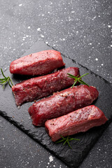 Raw beef steak. Raw fresh farm steak on black board on dark grey background. Raw beef steak for cooking vertical photo