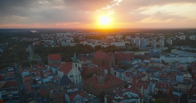 A wide aerial drone orbit of Toruń's historic Old Town Square at sunset. The camera tilts down to reveal the bustling market square, capturing the golden light on the rooftops and the iconic Town Hall