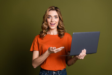 Cheerful young woman with curly hairstyle smiling and holding laptop against green background presenting content