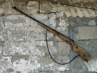 An old wooden rifle, hanging on a rough, whitewashed brick wall, is a symbol of hunting, guarding, or past conflicts. Its worn appearance and simple design emphasize the authenticity and history of th