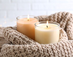 Two candles in glass holders, nestled in a cozy knitted blanket