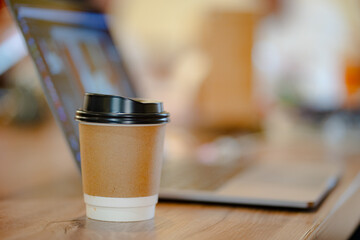 Close up cup of hot coffee with blurred laptop and mobile table at office or cafe, mock up concept.