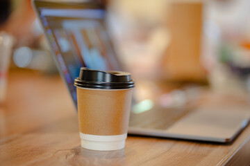 Close up cup of hot coffee with blurred laptop and mobile table at office or cafe, mock up concept.