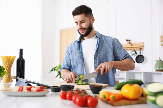 Smiling man looking at recipe on tablet while cooking at table in kitchen
