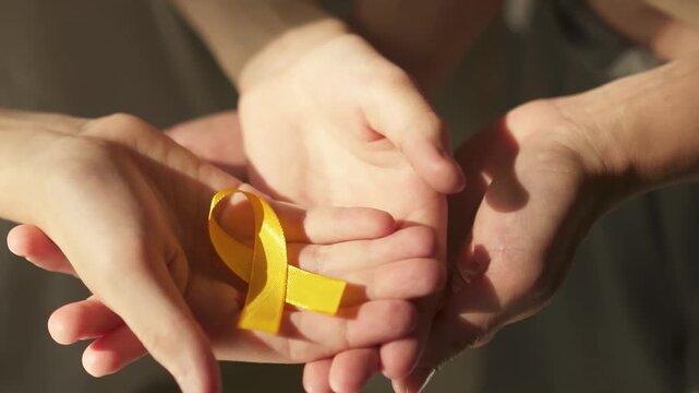 Powerful image of protective hands encircling small hands holding yellow ribbon, symbolizing unity in childhood cancer support.