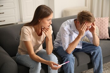 Worried couple with pregnancy test on sofa at home