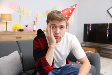 Man suffering from hangover on sofa in messy room after party