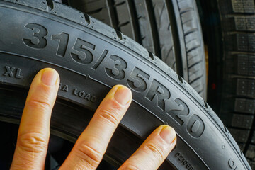 Close-up of car tire sidewall with size marking and hand pointing at tire size specifications © Zigmunds