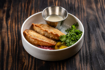 Fried empanadas with sauce and herbs in bowl.