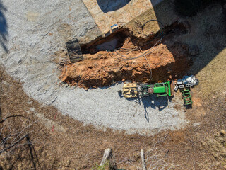 Aerial top down of tractor digging up septic tank in winter in driveway in winter