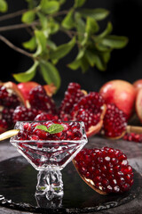 Fresh Pomegranate Seeds in Crystal Bowl with Whole Fruits Display on Rustic Wood