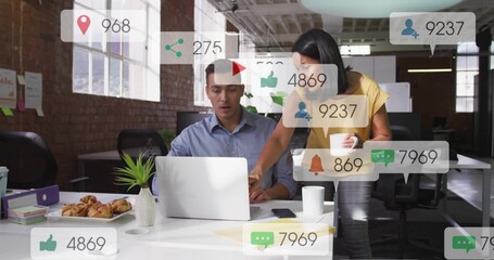 Working man in blue shirt consulting colleague at open-plan office, with laptop and social metrics